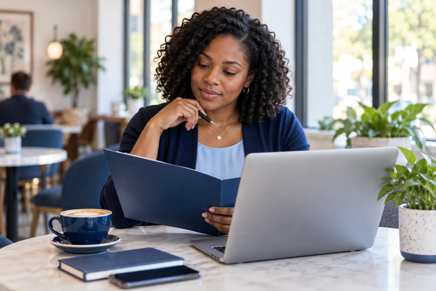 A woman reviewing a folder beside her laptop in a cafe.