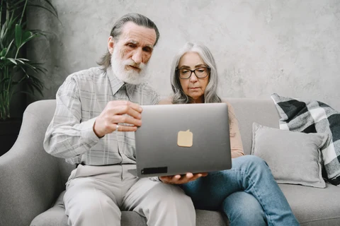 An older couple sits on a sofa looking at a laptop together.