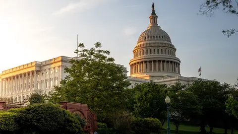 The United States Capitol at sunrise beneath a blue sky.