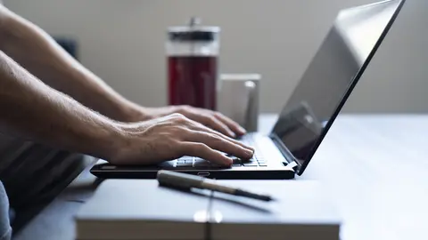 Hands typing on a laptop beside a notebook