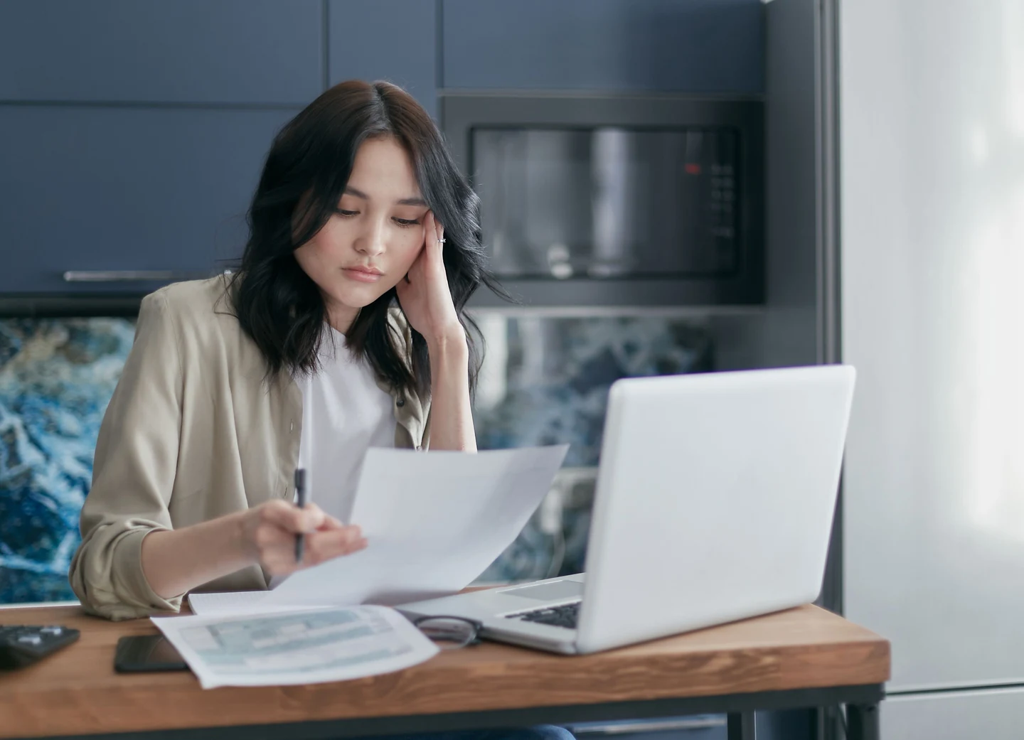 A woman reviews paperwork beside an open laptop at a table.