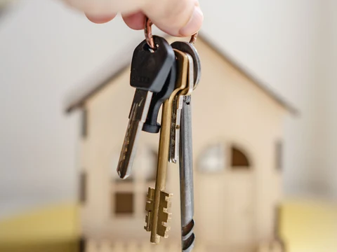 House keys hang in front of a small wooden house model.